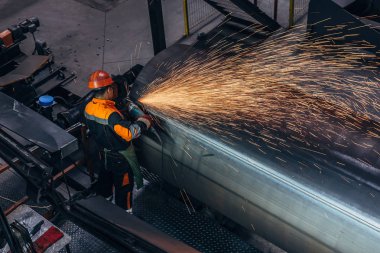İşçi, çelik boru üzerindeki kaynaklı dimi taşlama makinesi i kullanarak temizler