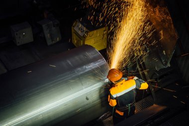 İşçi, çelik boru üzerindeki kaynaklı dimi taşlama makinesi i kullanarak temizler