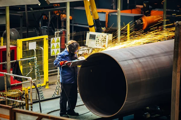 Worker cleans welded seam on steel pipe using grinding machine i