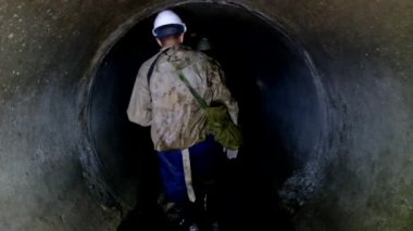 Kanalizasyon işçisi kanalizasyon tünelinden geçiyor.
