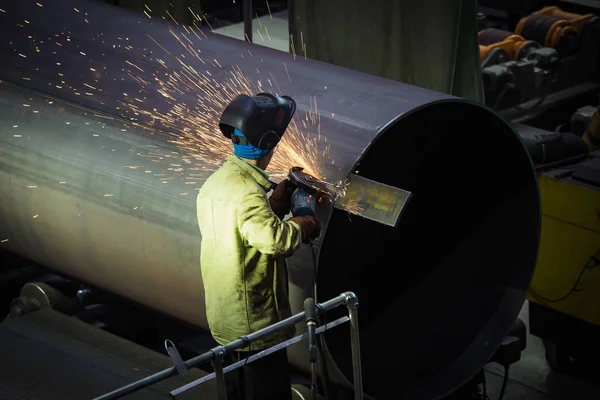 Worker cleans welded seam on steel pipe using grinding machine i