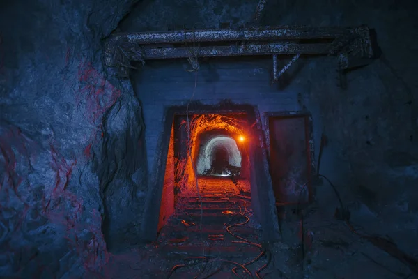 Dark dirty abandoned uranium mine with rusty remnants of railway color illuminated — Stock Photo, Image