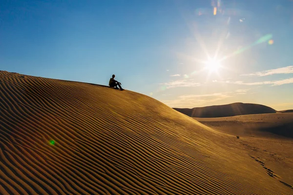 Petite silhouette de l'homme assis dans la dune du désert de sable au coucher du soleil — Photo