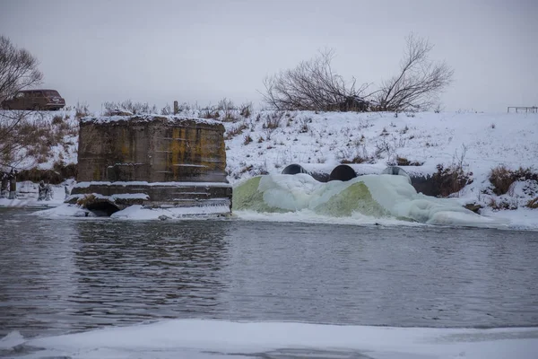 Frozen dirty sewage stream flowing from sewer pipe