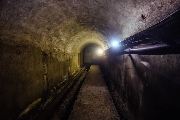 Gewelfde ondergrondse tunnel met elektrische kabels en roestige hea — Stockfoto