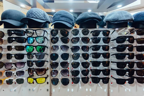 Diferentes gafas de sol multicolores de moda y gorras en la tienda — Foto de Stock