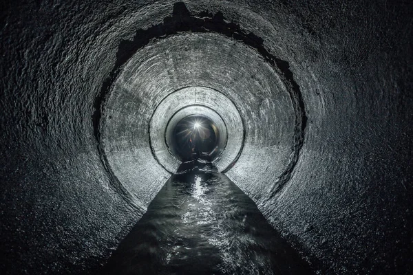 Underjordisk flod som rinner i en rund betongavloppstunnel. Avloppsvatten — Stockfoto