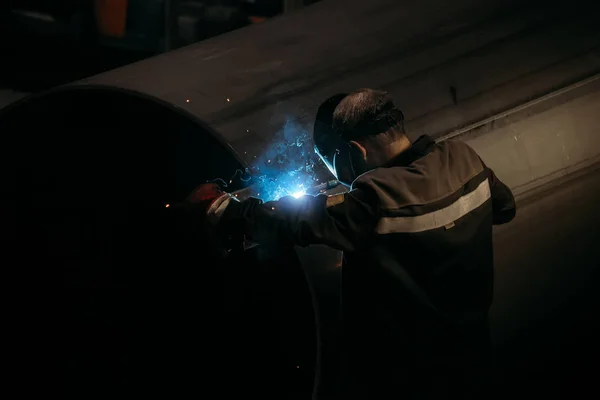 Worker in protective mask welding pipe in factory