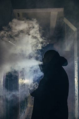 Karanlık, kasvetli koridorda sigara içen ya da buharlaşan adam silueti. 