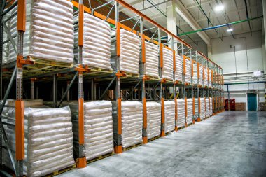 Fabrika yapımı tamamlanmış beyaz polietilen çantalı raflarla dolu bir hangar deposu.