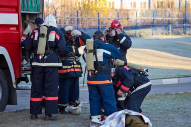 Bir grup itfaiyeci gaz maskesi takıp yangını söndürmeye hazırlanıyor.