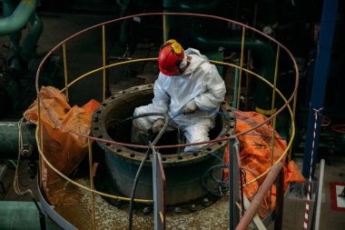 İşçi büyük çelik tankın boru bağlantılarını tamir ediyor