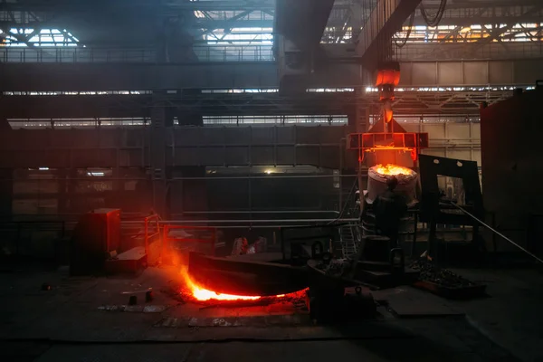 Worker operates metal casting process in metallurgical plant.