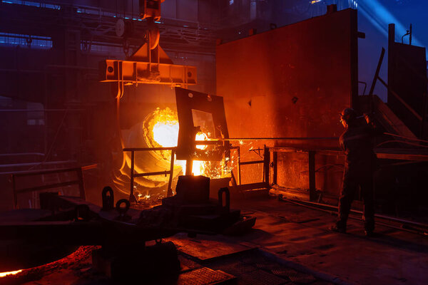 Worker operates metal casting process in metallurgical plant.