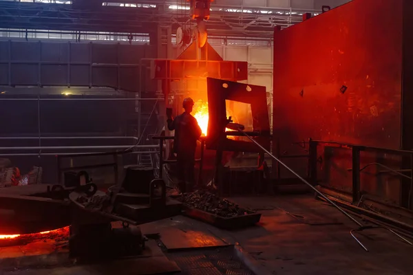 Worker operates metal casting process in metallurgical plant.