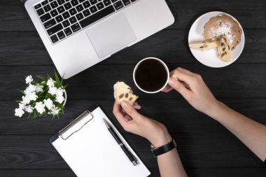 Kadın eli bir fincan kahve ve siyah arka planda kek.