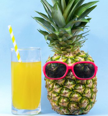 Mavi arka planda bir bardak meyve suyu ve ananas.