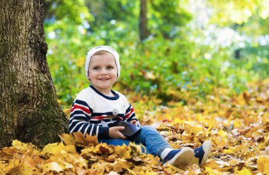 Çocuk elinde telefonla bir ağacın altında oturuyor.