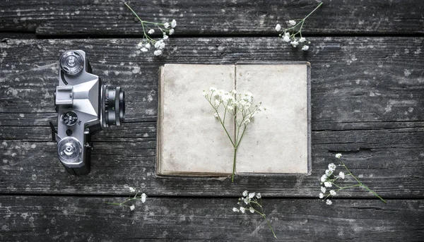 Photo camera, diary and flowers on a wooden backgroun