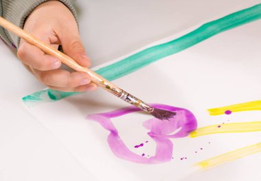 Çocuğun eli fırçayla sarı resim çiziyor.