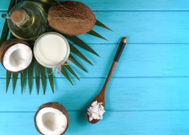 Ahşap bir kasede hindistan cevizi parçaları ve mavi arka planda hindistan cevizi talaşı ve hindistan cevizi yağı.