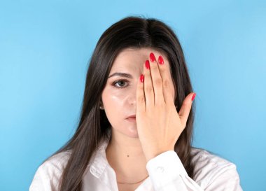 Genç esmer kadın bir gözünü eliyle kapatıp kameraya bakıyor. Fotokopi alanı ile mavi arkaplan üzerinde ön portre