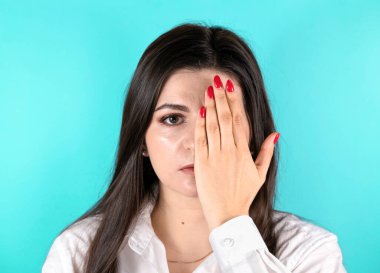 Genç esmer kadın bir gözünü eliyle kapatıp kameraya bakıyor. Fotokopi alanı ile mavi arkaplan üzerinde ön portre