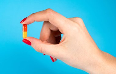 Mavi arka planda tek sarı morina yağı kapsülü tutan kadın.