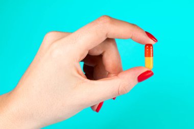 Mavi arka planda tek sarı morina yağı kapsülü tutan kadın.