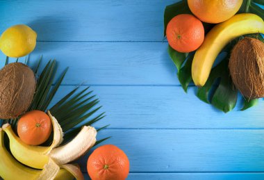 Mavi ahşap arka planda egzotik tropikal meyve ve palmiye yaprakları grubu.