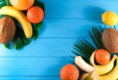 Mavi ahşap arka planda egzotik tropikal meyve ve palmiye yaprakları grubu.