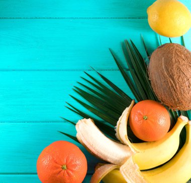 Yeşil ahşap zemin üzerinde egzotik tropikal meyve ve palmiye yaprakları grubu.