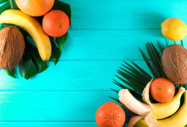 Yeşil ahşap zemin üzerinde egzotik tropikal meyve ve palmiye yaprakları grubu.