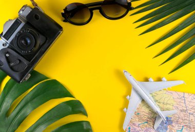 Gezgin aksesuarları, tropikal palmiye yaprağı ve sarı zemin üzerinde metin için fotokopi alanı olan uçak üst görünümü