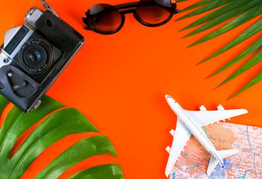 Turuncu zemin üzerinde gezgin aksesuarları, tropikal palmiye yaprağı ve uçak üst görünümü metin için kopya alanı