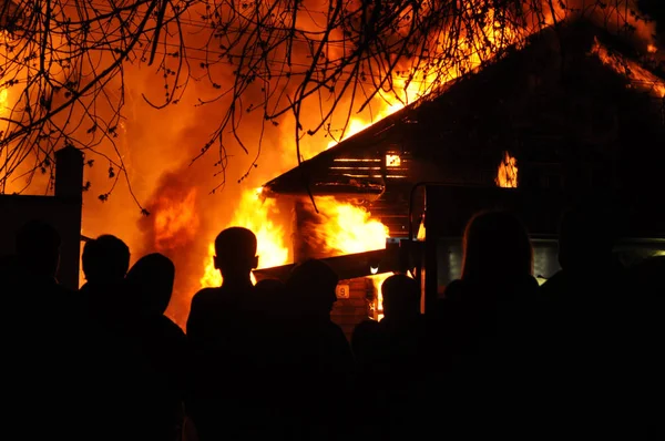 Pessoas olhando uma velha casa de madeira queimando — Fotografia de Stock