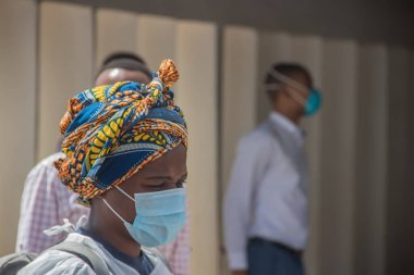 Korona-covid-19 saatinde koruyucu maske takan Afrikalı kadın, arka planda maskeli birkaç kişi.. 
