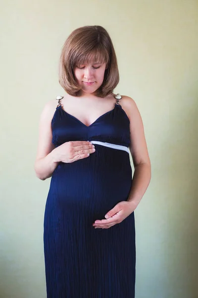 Pregnant woman caressing her belly over  green wall — Stock Photo, Image