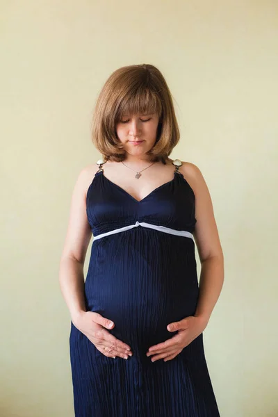 Pregnant woman caressing her belly over  green wall — Stock Photo, Image