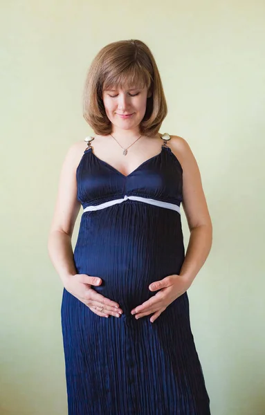 Mujer embarazada acariciando su vientre sobre la pared verde —  Fotos de Stock