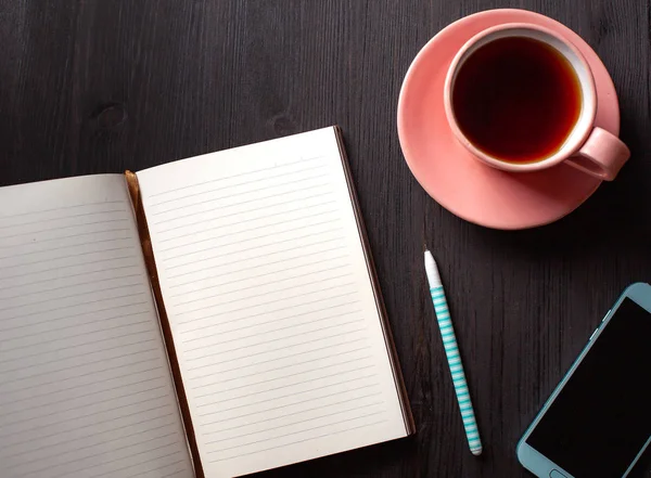 Primer plano del cuaderno abierto, taza de té, pluma y teléfono sobre fondo negro —  Fotos de Stock