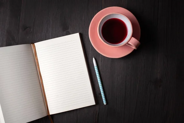 Planer aberto, xícara de chá, caneta em um fundo preto — Fotografia de Stock