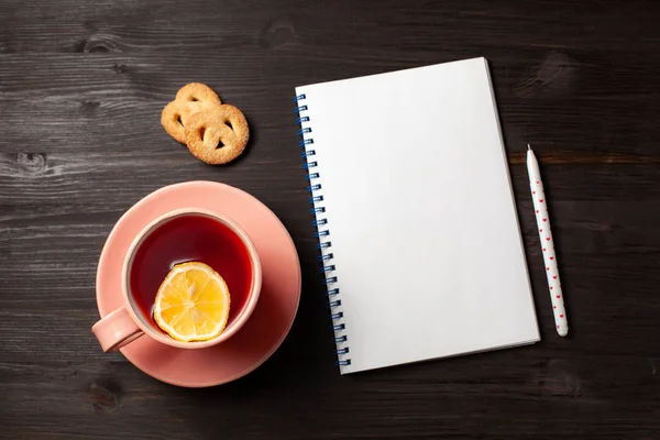 Aufgeschlagenes Lesebuch, eine Tasse Tee, ein Stift auf schwarzem Holzgrund — Stockfoto