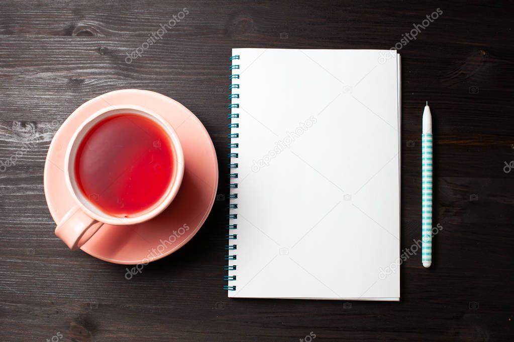 Open notebook, cup of tea, pen on black background