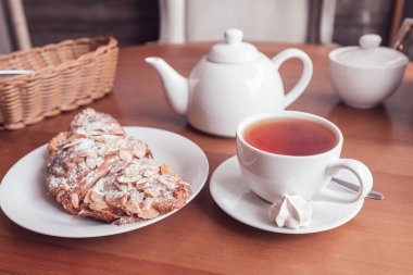 Kahve masasında çay fincanı, çaydanlık ve kruvasan.