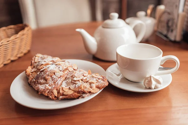 Xícara de chá, bule e croissant na mesa no café — Fotografia de Stock