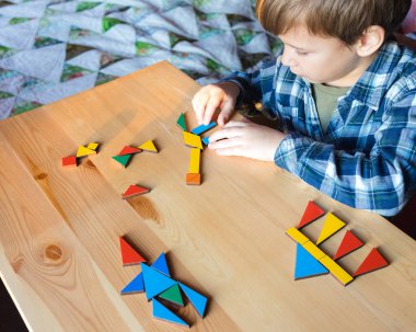 Çocuk masada oturur ve geometrik şekillerin resimlerini dizer.
