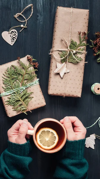 Kotak hadiah Natal dibungkus kertas kraft. Womans tangan memegang cangkir dengan teh — Stok Foto