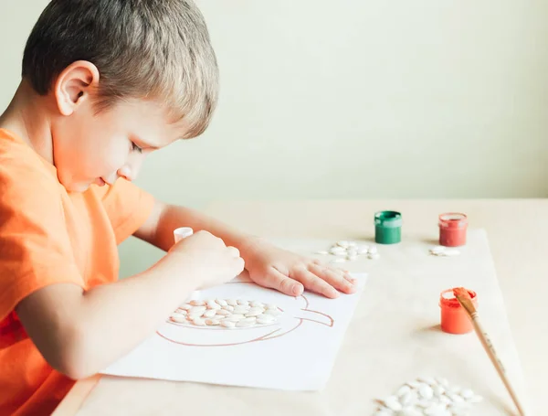 Anak manis membuat labu dari biji di atas kertas putih, konsep Halloween DIY — Stok Foto