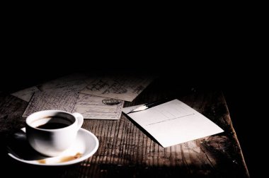 Tahta bir masada eski kartpostallar, kahve fincanı ve kalem.